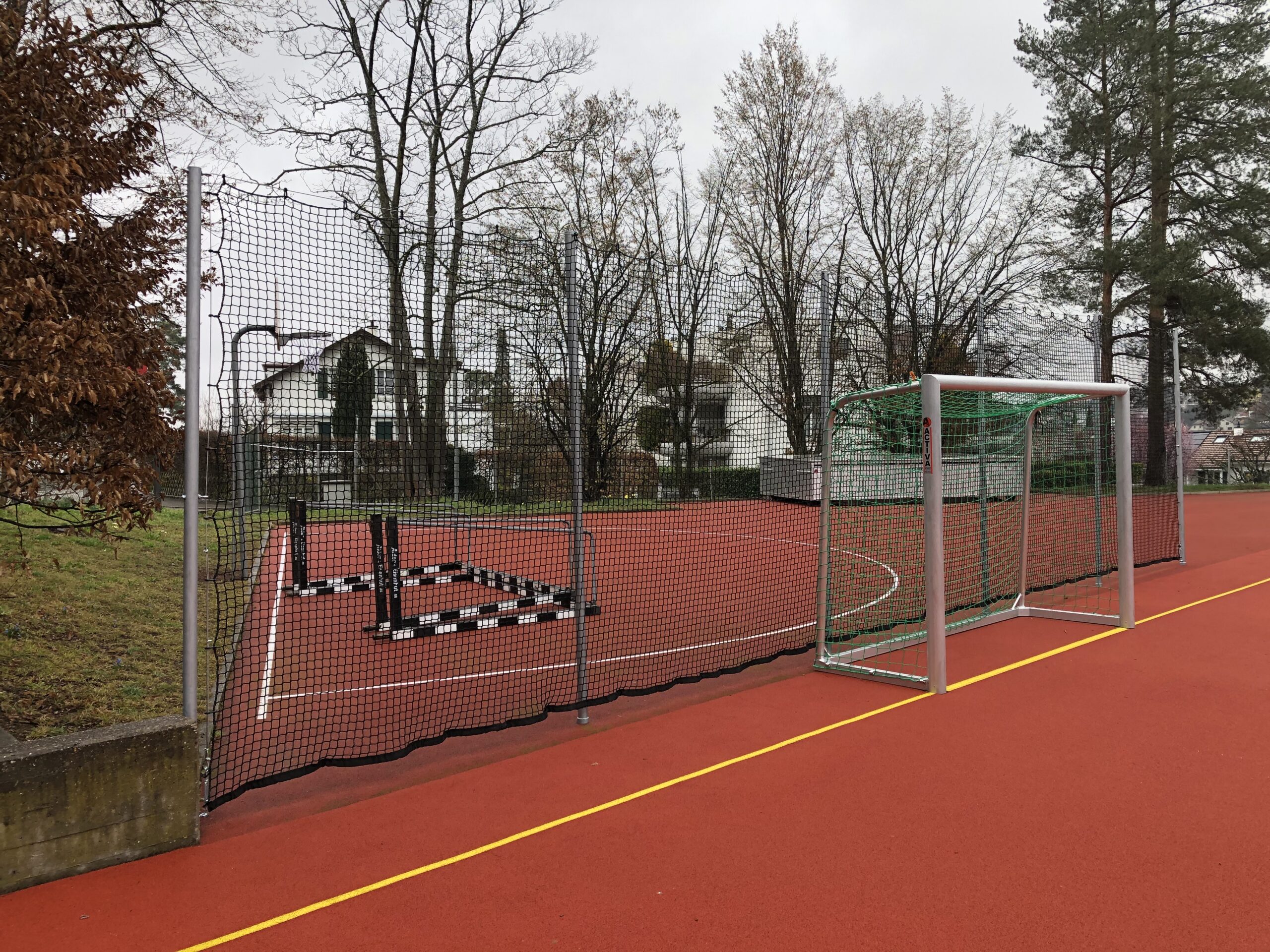 Schutznetz gespannt an Bleischnur, mit Pfosten, auf Sportplatz, roter Tartanbelag