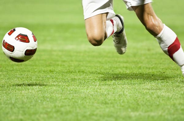 Willkommen bei Activa Sport, ein Fussballspieler läuft mit dem Ball auf dem Rasen